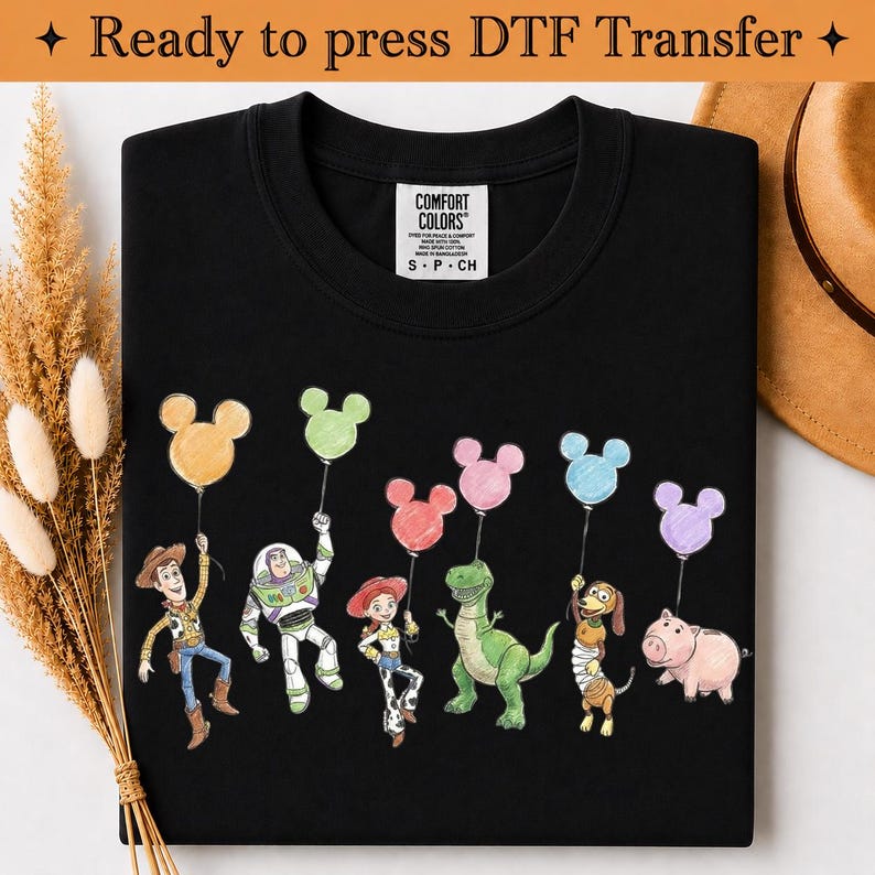 Puede incluir: Una camiseta negra con un estampado gr&aacute;fico de seis personajes animados, cada uno sosteniendo un globo con forma de Mickey Mouse en varios colores pastel. La camiseta tiene una etiqueta interior blanca con el texto Comfort Colors S P CH.
