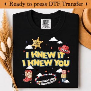 May include: A black t-shirt featuring a graphic print with the text I KNEW IT I KNEW YOU, a yellow sheriff star with the text INFINITY AND BEYOND, a red cowboy hat, red cowboy boots, a beaded bracelet with the text YOU'VE GOT A FRIEND IN ME, and blocks.