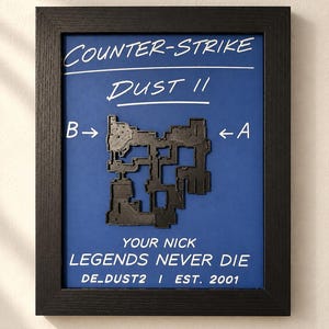 May include: A framed wall art piece featuring a blue background with white text reading COUNTER-STRIKE DUST II, YOUR NICK, LEGENDS NEVER DIE, DE_DUST2, and EST. 2001. A black 3D-printed map of the game level is centered with B and A site markers.