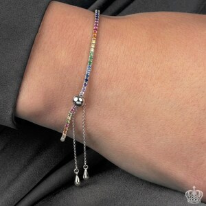 May include: A silver bracelet with a row of colorful gemstones. The gemstones are arranged in a rainbow pattern. The bracelet has a sliding clasp and two small dangling charms.