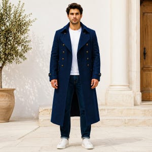 May include: A long, double-breasted navy blue wool coat with wide lapels and dark buttons, worn over a plain white crew-neck t-shirt and dark blue denim jeans, paired with simple white sneakers. The coat features structured shoulders and long sleeves.