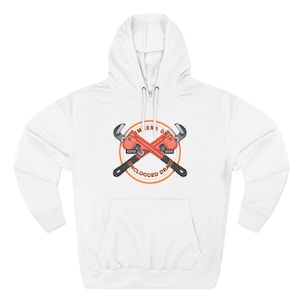 Könnte beinhalten: Weißer Kapuzenpullover mit Fronttasche und Kordelzug. Das Design zeigt zwei gekreuzte rote Rohrzangen mit dem Text "PLUMBERS DRIP" und "UNCLOGGED DRAIN" in einem kreisförmigen Emblem. Das Emblem enthält auch den Text "ESTD 2026".