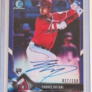 May include: A baseball card featuring Shohei Ohtani in a red Angels uniform, swinging a bat. The card has a blue background with the text "Chrome" and "RC". It is numbered 017/150 and includes an autograph.