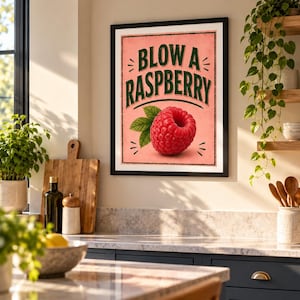 Peut inclure: Une affiche murale encadrée sur fond rose avec le texte BLOW A RASPBERRY en lettres capitales vert foncé. Sous le texte se trouve une illustration détaillée d'une framboise rouge unique avec deux feuilles vertes, le tout dans un cadre noir.