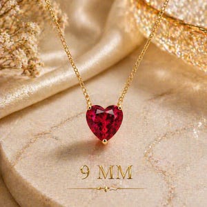 Op de afbeelding: Een gouden ketting met een gefacetteerde, hartvormige rode edelsteen hanger. De hanger is duidelijk gemarkeerd als 9 mm. De ketting is voorzien van een fijne gouden schakelketting en een levendige rode steen in een gouden zetting.