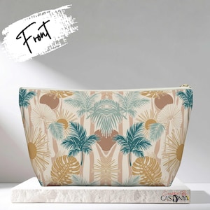 May include: A beige cosmetic bag with a tropical pattern featuring palm trees, suns, and leaves in teal, brown, and gold. The bag has a gold zipper and the word "Front" is written on the top left.
