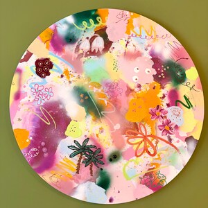 Könnte beinhalten: Ein rundes, abstraktes Gemälde mit einer lebendigen Farbpalette. Das Kunstwerk zeigt rosa, gelbe, orange und grüne Farbtöne mit floralen und Palmenmotiven. Das Gemälde hängt an einer grünen Wand.