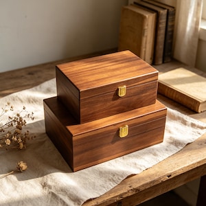 Pu&ograve; includere: Due scatole rettangolari in legno impilate l'una sull'altra, realizzate in legno marrone scuro con venature visibili. Ogni scatola presenta una chiusura in metallo color oro lucido centrata sul pannello frontale per una chiusura sicura.