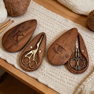 May include: Wooden scissor cases with decorative gold and bronze scissors. One case is engraved with "Kaser's Tools", another with "Rocco" and a knitting design. The scissors are designed for crafting and sewing.