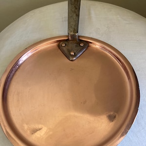 Op de afbeelding: Een ronde koperen koekenpan met een geklonken metalen handvat. De pan heeft een iets verhoogde rand en het nummer "20" is op het oppervlak gestempeld. Het handvat heeft een gat om op te hangen. Een vintage keukenartikel.