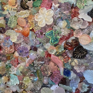 May include: A large collection of assorted acrylic and glass beads in various shapes, including flowers, butterflies, hearts, and leaves. The beads feature a mix of translucent, opaque, iridescent, and solid colors like pink, blue, green, and clear.
