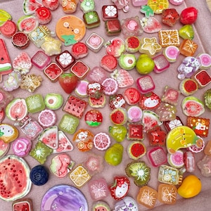 Könnte beinhalten: Eine Sammlung kleiner, bunter Harzanhänger in verschiedenen Fruchtformen, darunter Wassermelonenscheiben, Erdbeeren, Zitrusfrüchte und Kiwis, sowie verschiedene Zeichentrickfiguren und geometrische Formen in leuchtenden Farben.