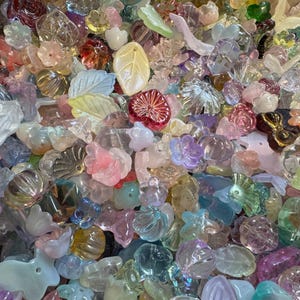 May include: A large collection of assorted translucent acrylic beads in various shapes including flowers, leaves, and hearts. The beads feature a pastel color palette with pink, blue, yellow, green, and clear tones, each with a smooth, glossy finish.