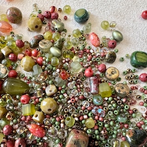 Puede incluir: Una gran colección de cuentas sueltas de diversas formas, tamaños y texturas, con una paleta de colores verde oliva, salvia, musgo, coral y rosa empolvado. El surtido incluye cuentas facetadas, redondas, cilíndricas e irregulares.
