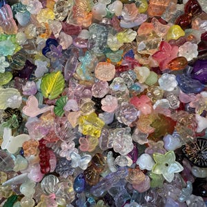 May include: A large collection of assorted translucent and opaque acrylic beads in various shapes including flowers, butterflies, and leaves. The beads feature a wide spectrum of colors such as pink, blue, green, yellow, purple, and clear finishes.