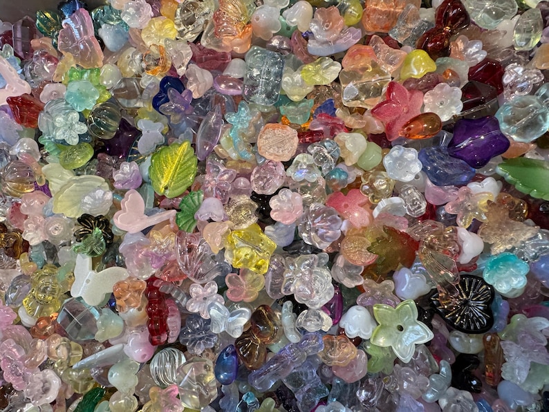 May include: A large collection of assorted translucent and opaque acrylic beads in various shapes including flowers, butterflies, and leaves. The beads feature a wide spectrum of colors such as pink, blue, green, yellow, purple, and clear finishes.