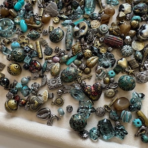 May include: A large collection of assorted jewellery beads and charms in various shapes, sizes, and textures. The assortment includes metallic gold, silver, and bronze pieces, along with turquoise, blue, and brown glass and stone beads.