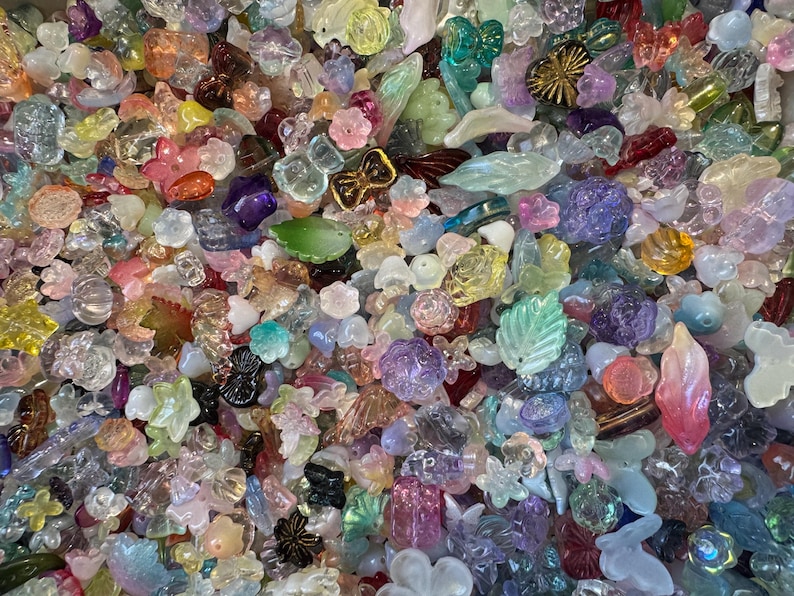 May include: A large collection of assorted translucent and opaque acrylic beads in various shapes including flowers, leaves, butterflies, and geometric forms. The beads feature a wide spectrum of pastel and vibrant colors with iridescent finishes.