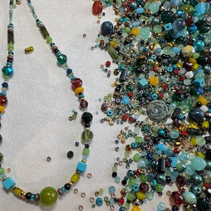 May include: A vibrant necklace featuring a mix of beads in various shapes and sizes, including green, red, yellow, and blue. A collection of loose beads in similar hues is scattered around the necklace.