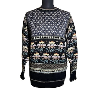 May include: A vintage sweater with a patterned design. The top portion features a diamond pattern in shades of gray and blue. The lower section showcases floral and geometric patterns in black, brown, and pastel colors. The cuffs and hem are solid black.