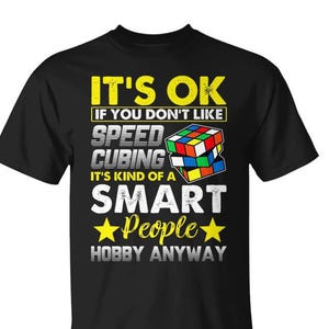 May include: A black short-sleeved t-shirt featuring a graphic with a colorful puzzle cube and the text: IT'S OK IF YOU DON'T LIKE SPEED CUBING IT'S KIND OF A SMART PEOPLE HOBBY ANYWAY. The design uses yellow, white, and grey lettering with two yellow stars.