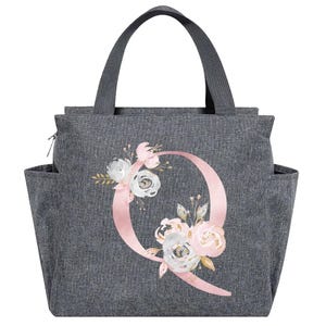 May include: Gray tote bag with a floral design and the letter "Q". The bag has a handle, side pockets, and a zipper closure. The floral design includes pink, white, and gold flowers.
