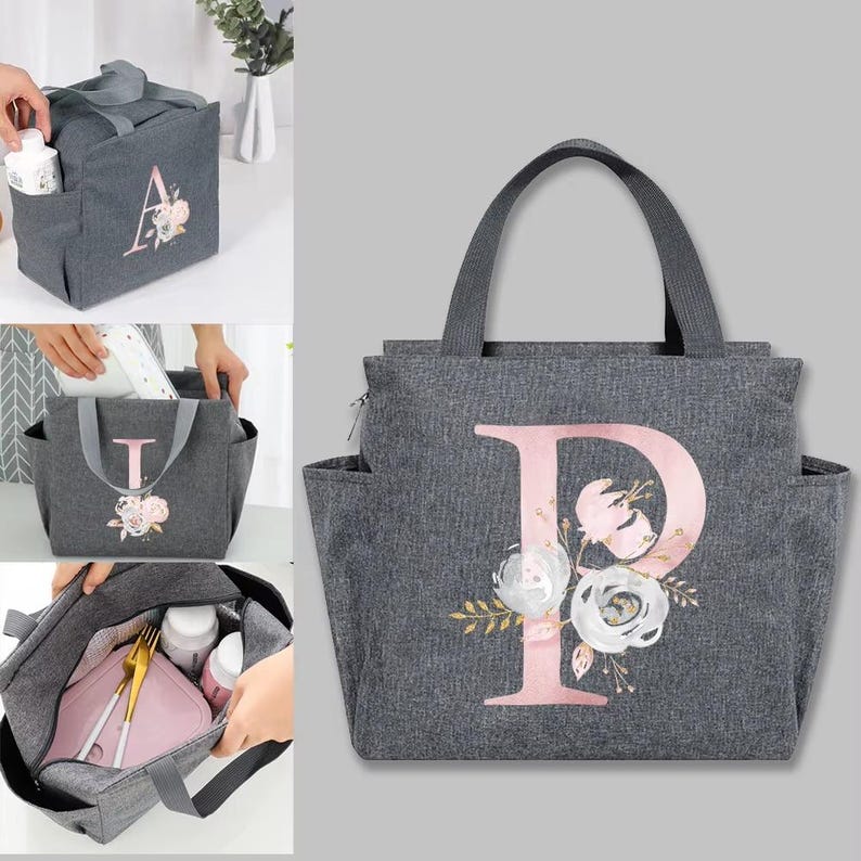 May include: Gray insulated lunch bag with a large pink letter "P" and floral design. The bag has a top handle, side pockets, and a zipper closure. The bag is designed to carry food and drinks.