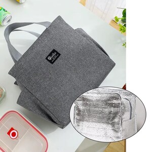May include: A gray insulated lunch bag with a matching handle. The bag has a rectangular shape and a small label that reads "Brinitas". The interior of the bag is silver. The bag is designed to keep food and drinks cold.