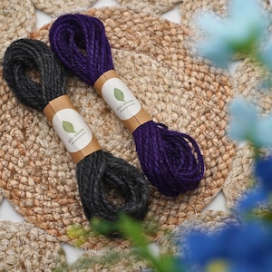 May include: Two bundles of twisted twine, one in dark charcoal gray and one in deep purple. Each bundle is secured with a tan paper band featuring a green leaf icon and the text ECO GRONN ecogronn.com printed in black ink on the front.