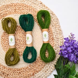 May include: Three bundles of twisted twine in olive green, dark forest green, and bright grass green. Each bundle is secured with a tan paper band featuring a white circular label with a green leaf icon and the text ECO GROWN.