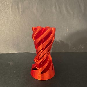 以下が含まれることがあります： 鮮やかな赤色の3Dプリント装飾品。ねじれたスパイラルデザイン。円筒形で、渦巻くリボンの間に空間がある。色は明るい赤色で、表面はわずかにテクスチャ加工されている。