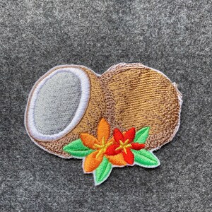 May include: Embroidered patch featuring a brown coconut with a gray interior and white border. Two flowers with orange and red petals and green leaves are on the bottom. The patch is on a gray background.