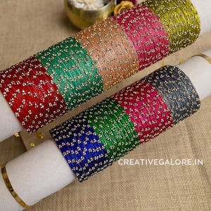 Puede incluir: Dos juegos de pulseras de cristal de colores, cada uno seccionado en diferentes colores, incluyendo rojo, verde, marrón, rosa y dorado. Las pulseras están adornadas con pequeños adornos plateados. El texto "CREATIVEGALORE.IN" es visible.