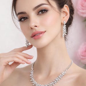 May include: A sparkling silver necklace and earring set. The jewelry features a floral design with numerous clear crystals. The earrings are long and dangle, while the necklace sits elegantly on the neckline. The set is perfect for special occasions.