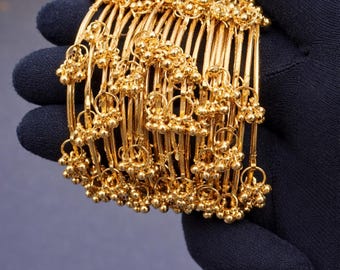 May include: A set of gold-toned metal bangles featuring thin, circular bands adorned with small, dangling spherical charms. The bangles are arranged in a stacked formation, showcasing a consistent metallic finish and uniform design across each piece.