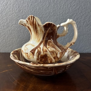 May include: A ceramic creamer pitcher and matching bowl set featuring a marbled pattern of dark brown and cream swirls. The pitcher has a curved handle and a scalloped pouring spout, while the bowl has a wide, shallow basin with matching colors.