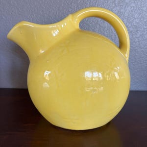May include: A white ceramic mug with a black handle and the text "But First, Coffee" in a black, bold font. The mug is on a white surface. The mug is 4 inches tall.
