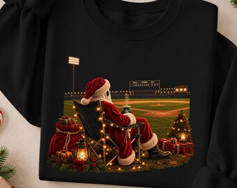 May include: A black crewneck sweatshirt featuring a graphic of Santa Claus sitting in a folding chair on a baseball field at night, holding a mug. The scene includes a scoreboard, a small lit Christmas tree, and wrapped gifts.