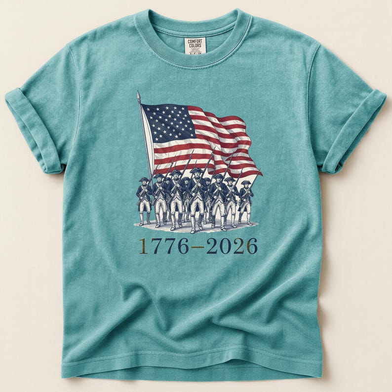 May include: Teal-colored t-shirt featuring a vintage illustration of soldiers carrying the American flag. The flag is red, white, and blue. The text "1776-2026" is printed below the image. The shirt is made of Comfort Colors material.
