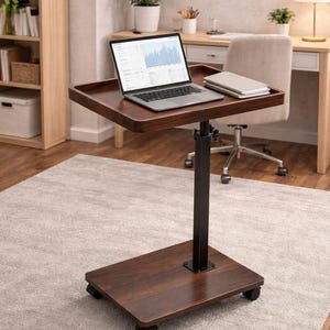 May include: A dark brown, rolling laptop desk with a black metal frame. The desk has a rectangular top with a raised edge, holding a laptop and a notebook. The base is also rectangular and rests on four wheels.