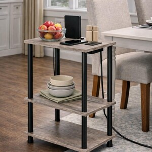 May include: A three-tiered side table with a gray wood-look finish and black metal legs. The top shelf holds a glass bowl of fruit, a black device, a phone, and wooden salt and pepper shakers. The middle shelf has bowls and a green cloth.