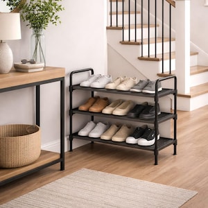 May include: A three-tiered black metal shoe rack filled with various pairs of shoes. The shoes are in different colors, including white, beige, brown, and black. The rack is placed in a well-lit hallway with a wooden floor and a staircase in the background.