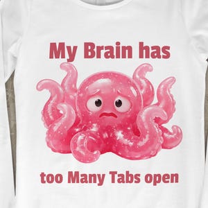 以下が含まれることがあります： ピンクのタコのデザインと「My Brain has too Many Tabs open」の文字が入った白い長袖Tシャツ。タコは悲しそうな表情をしています。このシャツは柔らかい素材で作られています。