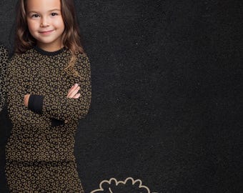 May include: A long-sleeve shirt and pants set featuring a brown and black leopard print pattern with solid black cuffs and neckline. The text COMFY, NEVER TAME! is displayed above, and a line art illustration of a lion is below.