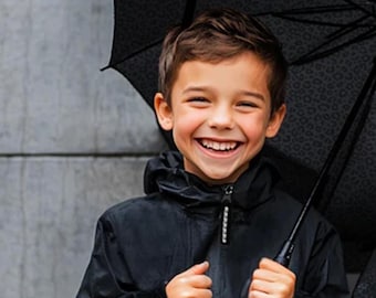 May include: A smiling child wearing a black hooded jacket and holding a black umbrella with a leopard print pattern. The umbrella is open, and the child is looking at the camera.