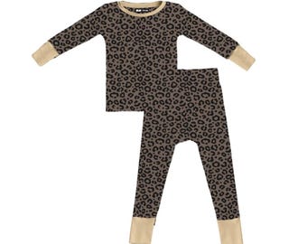 May include: A two-piece pajama set featuring a long-sleeve top and matching pants with a brown and black leopard print pattern. The garment includes solid tan ribbed cuffs at the wrists and ankles, and a tan ribbed crew neckline.