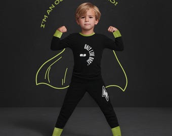 May include: A black long-sleeve shirt and pants set with lime green cuffs and collar. The shirt features the text "ONLY LIVE ONCE" and a logo. The pants have a white lightning bolt graphic. A lime green outline of a cape and the text "I'M AN OLO SUPERHERO!" appear behind.