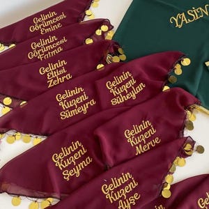 Puede incluir: Varios pañuelos burdeos con texto y ribetes dorados, cada uno con un nombre diferente. También se ve un pañuelo verde con texto dorado. El texto parece estar en turco.
