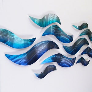 May include: Abstract wall art sculpture made of metal with a blue and green color scheme. The sculpture is made up of multiple pieces that are arranged in a wave-like pattern.