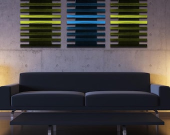 May include: Three abstract wall art pieces in a modern living room. The pieces are made of wood slats in shades of green, blue, and yellow. The pieces are hung on a gray concrete wall above a black couch.
